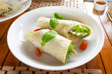 Tortilla wrap with chicken meat and vegetables on traditional dish topping with spinach.