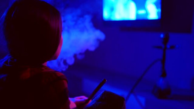 Girl watching TV, blue and red room lighting, smoking a hookah