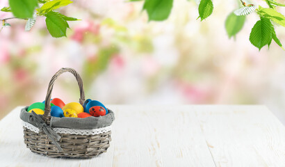 Easter eggs in a basket on white wooden table on blurred floral bakground. Copy space