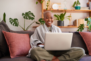 A young woman sits on the couch with her laptop and smiles