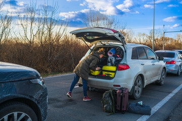 A refugee from Ukraine puts things in the trunk of a car in a convoy of cars in front of the...