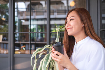 Portrait image of a beautiful young asian woman holding and drinking hot coffee in paper cup
