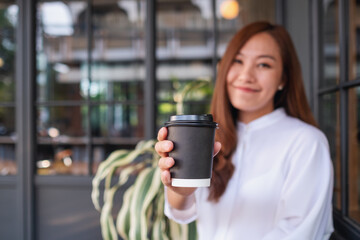 Blurred image of a beautiful young asian woman holding and drinking hot coffee in paper cup