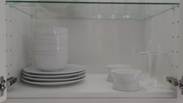 Opening closing the kitchen cabinet glass door with crockery shelves illuminated from the inside. Closeup details of kitchen furniture. High quality 4k footage