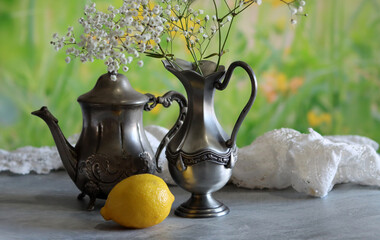 Still life with vintage silver teapot and pitcher, white gypsophila flowers, lemon and blue and...
