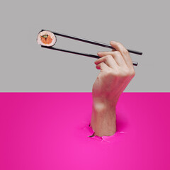 Man hand holding black chopstick with one piece rice salmon and cucumber roll in nori dried edible seaweed. Sushi eating minimal concept. Pink and gray background