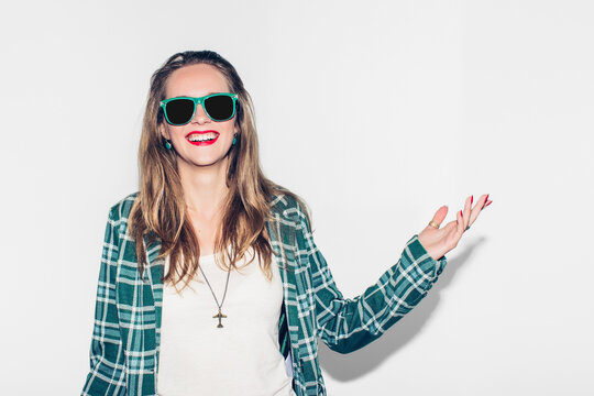 Young beautiful long-haired urban happy hipster girl in green checkered jacket and sunglasses having fun, laugh and wide smile with perfect teeth. White background.