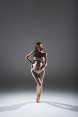 Full length of pregnant woman in panties and top standing on grey background