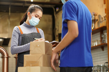 Waitress wearing mask check the box from food supply delivery man to restaurant pick up point and take away from online order as new normal while coronavirus or COVID-19 outbreak