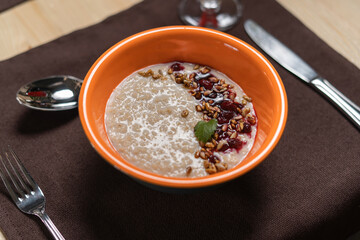 Oatmeal porridge in a orange porcelain bowl with jam and seeds.