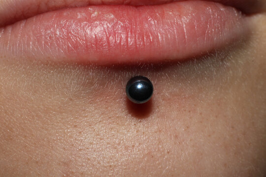 Girl lower lip piercing.
Labret piercing. Macro.
Blue ball.