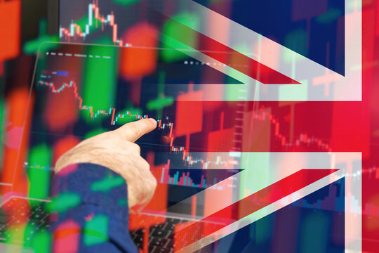 UK downtrend of the economy in a world crisis. Man hand shows on the decreasing candle stick graph chart in the stock market with the flag on the background, March 2022, San Francisco, USA