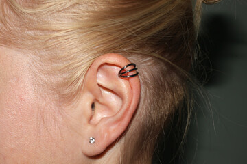 Girl's ear. Ear cartilage piercing + triple ring. Ear lobe piercing + transparent cubic zirconia.