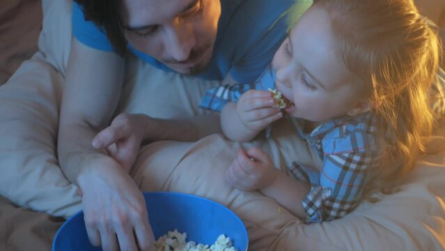 happy family, dad and daughter watch TV, eat popcorn, love each other. Fun games, leisure, indoor, evening. top