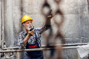 A senior factory worker speaking on talkie-walkie and pointing where to put freight.