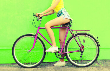 Fototapeta na wymiar Summer image of legs of beautiful young woman in shorts posing with bicycle in the city on green background