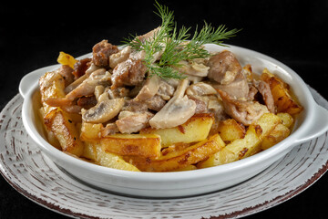Rustic potatoes with meat and mushrooms. In a plate on a black background.