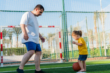Full body positive man playing soccer with little daughter kicking ball on green lawn. Father's Day concept. Joy of life.