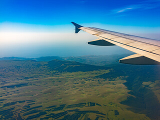 Obraz premium View of airplane wing, blue skies and green land during landing. Airplane window view.