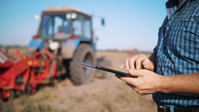 farmer is using digital tablet. close-up. on farm field, near tractor, on farm machinery backdrop. smart farming. farming technologies