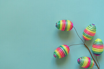 Top view mockup of multicolored rainbow striped eggs placed on branch on blue background 