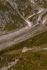 Majestic alpine landscape in the Lord of the Rings style. In the foreground is a grassy expanse with a path running across it towards the high mountains in the background, which overlook the scene.