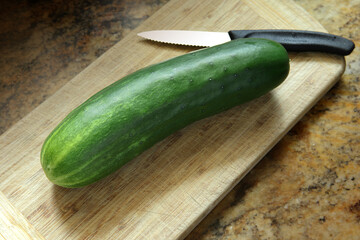 Long whole green cucumber on a wood cutting board with a knife close up