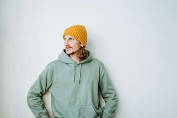 A man stands on a white background, hands put to his pocket, a hipster in a yellow hat, a casual style of clothing green sweatshirt.