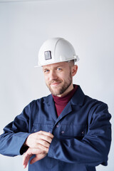 Construction industry concept. Attractive bearded caucasian engineer, worker, supervisor or building contractor in white helmet and blue uniform looking checking time. High quality vertical image