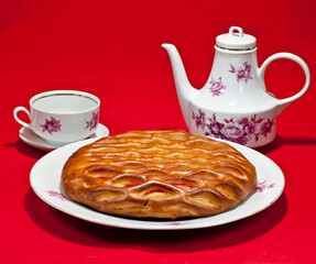 On the table on a red tablecloth, a cup of tea and a delicious national gata with strawberry jam