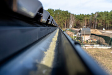 A metal, black gutter on a roof covered with ceramic tiles in the background a forest, view from above.