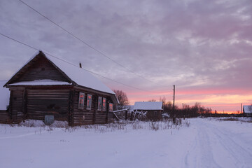 Winter, white snowdrifts, side view of a wooden house at sunset, pink sky, sunset, village, snow.