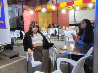 Two women sitting on a food stall on a night fair while eating fast food
