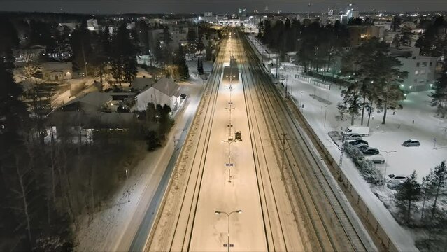 Vantaa.Finland-December 29.2021: Small tractors cleaning snow off of the train station platform in Vantaa. Maintaining transportation during the nordic winter. Aerial shot. Drone moving forward. 