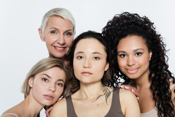Obraz premium Smiling interracial women hugging tattooed friend isolated on grey, feminism concept.