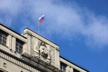 Russian flag on the parliament building in Moscow on background of blue sky and white clouds....