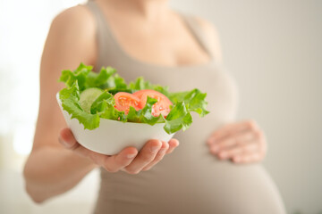 Pregnant woman is holding fresh vegetables in her hand. The concept of healthy eating during...