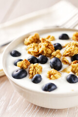 Yogurt with granola, nuts and blueberries in a ceramic plate on the white kitchen table