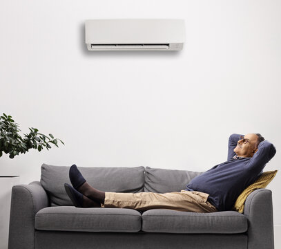 Mature man resting on a sofa under an air conditioning unit