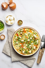 Flat lay egg frittata omelet with seasonal vegetables and cheese in plate on white marble background. Healthy breakfast food concept. Top view