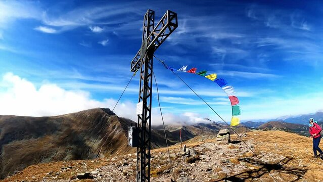 Woman and summit cross of mount Seckauer Zinken in the Seckau Tauern in Styria, Austria. Nepalese or Tibetan prayer flags are attached to it and strong wind is blowing. Freedom in the Austrian Alps
