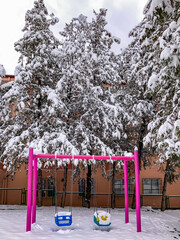 Blue swing with pink posts on playground covered with snow in winter. Selective focus.