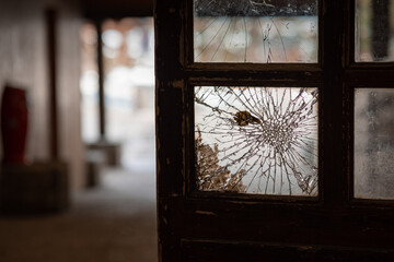 Broken glass or shattered window in a wooden frame of a door. Dark alley with destroyed window.