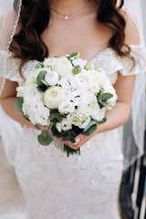 The bride in a white dress holds a luxurious bouquet of white peonies