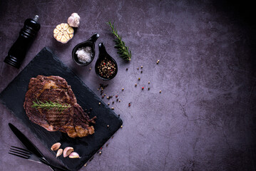 Sliced beef ribeye steak, grilled with 4seasons pepper garlic-rosemary, on stone plate dark and dark grey background, knife and fork black, top view