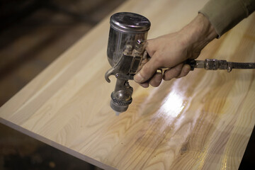 Applying varnish to board. Spray gun for paint supply. Instrument is in hand of man. Wood...