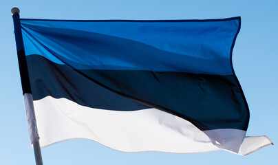 Close-up of flag of Estonia on blue sky background. Estonian flag waving in wind and sunlight. 