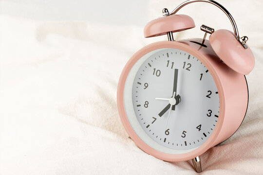 Morning concept. Classic pink alarm clock on the white wrinkled bed sheets close up image.