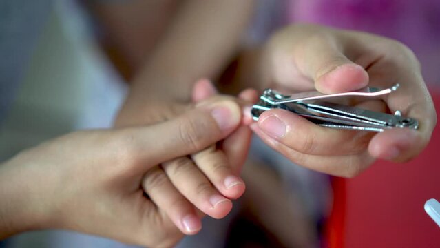 Close up view mother hand use nail clipper cut the nail of daughter