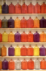 many colored glass bottles red orange violett in 3 lines on a shelf 